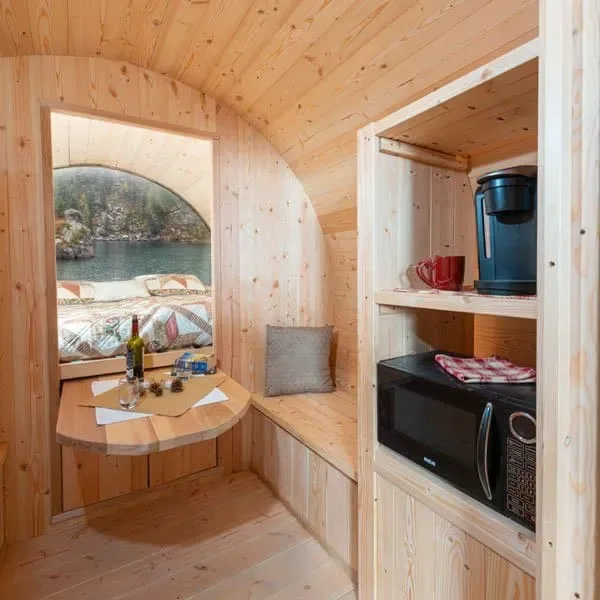 Inside a wood-lined barrel bunkie with a queen bed and round window