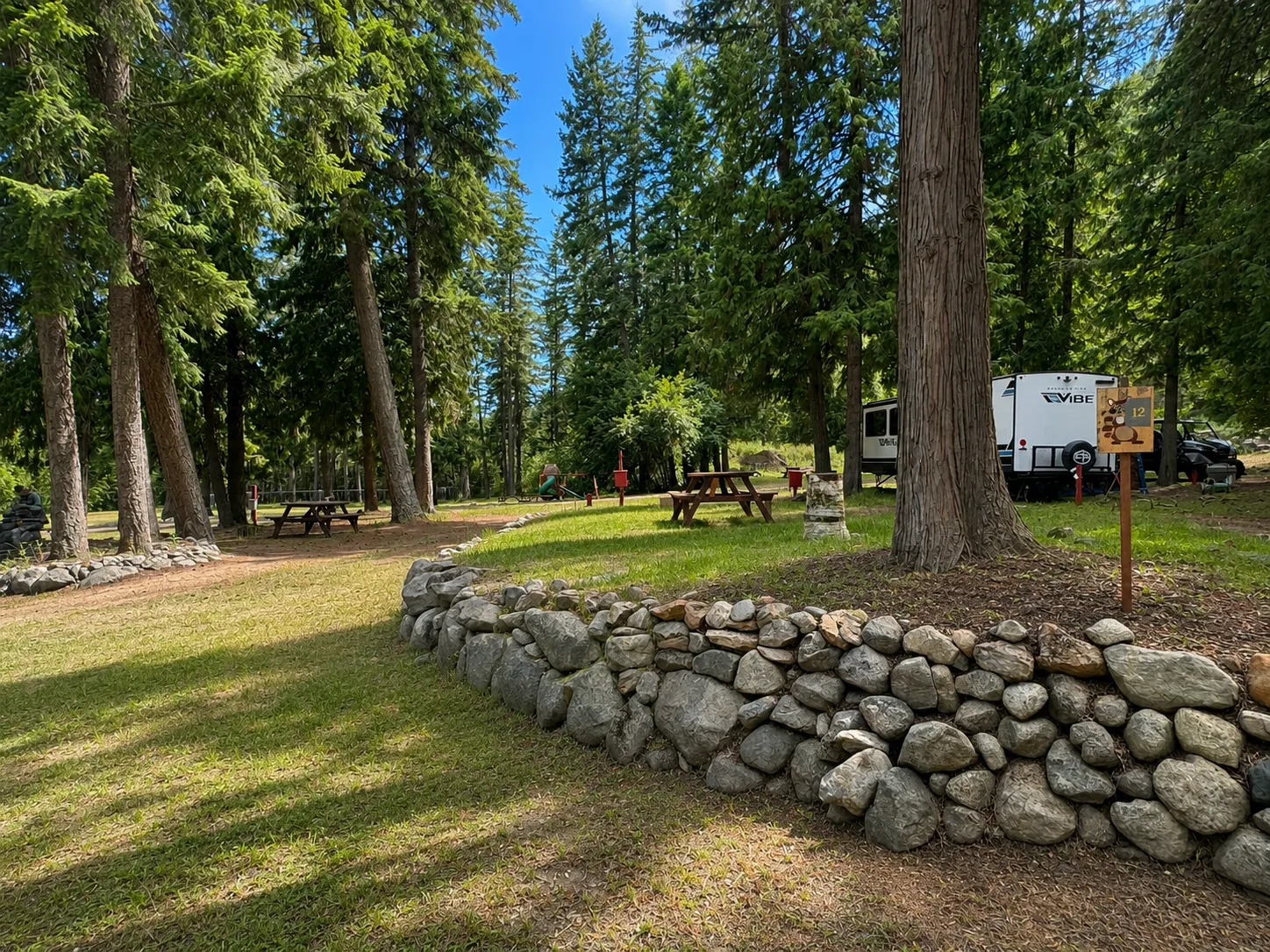 Forested RV sites with picnic tables and a stone retaining wall at Fox & Maple