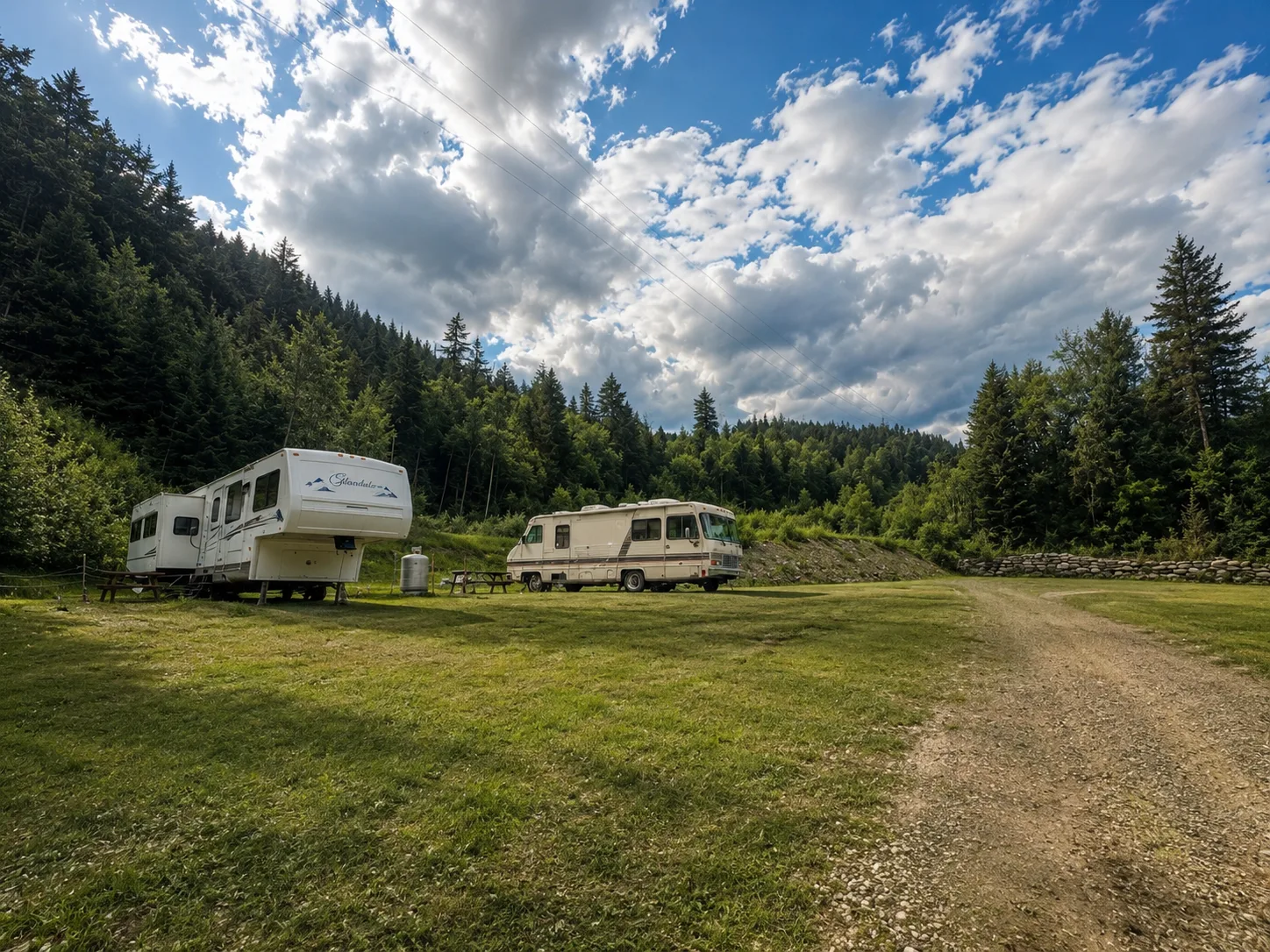 RVs parked on grassy long-term sites with forested hills behind