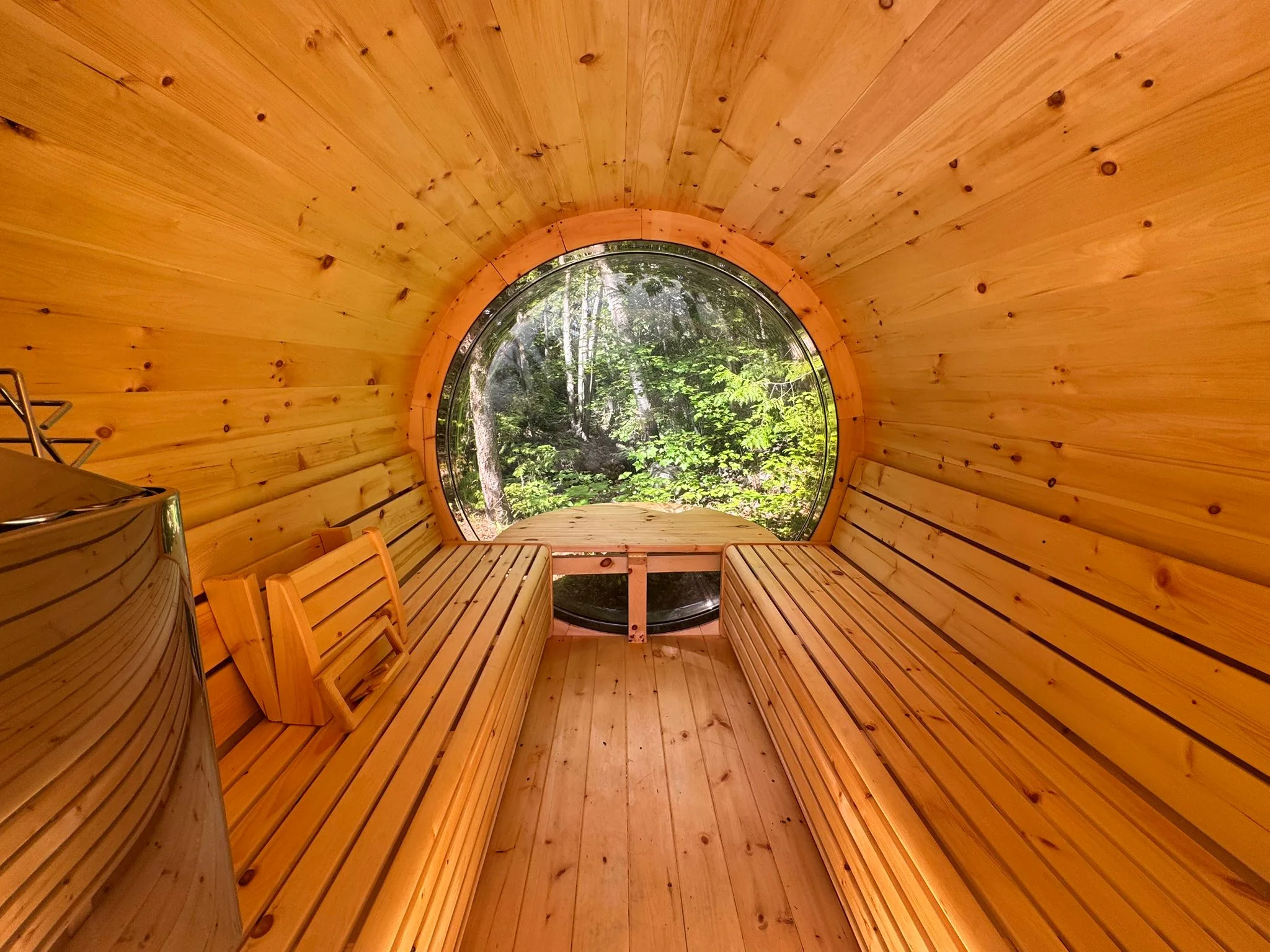 The electric barrel sauna lit up at dusk, surrounded by forest